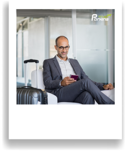 TrustParking-Ratgeber | Blog: Sicher und stressfrei am Flughafen Köln/Bonn: Regeln, die jeder kennen sollte (Lächelnder Mann im Anzug wartet entspannt mit Gepäck und Reisepass im Wartebereich eines Terminals)